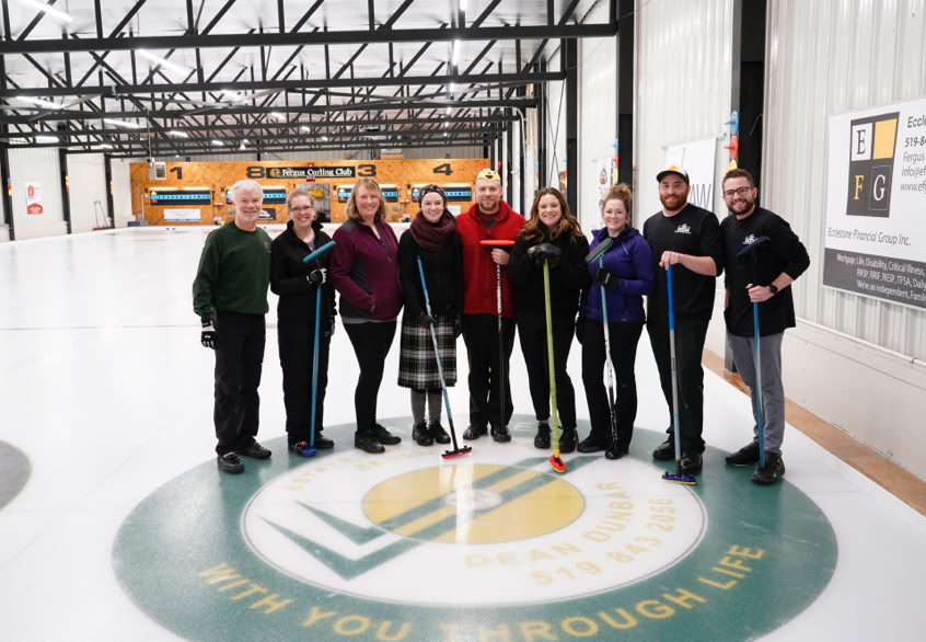 Nine Curl For A Cause particpants standing on curling rink ice surface.