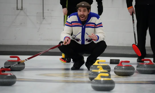 Curler squatting watching rock sliding across ice.