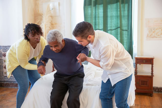 Two hospice volunteers assisting a resident to stand